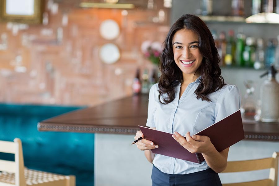 Specialized Business Insurance - Proud Restaurant Owner Holds a Reservation Book, Standing By a Modern Bar